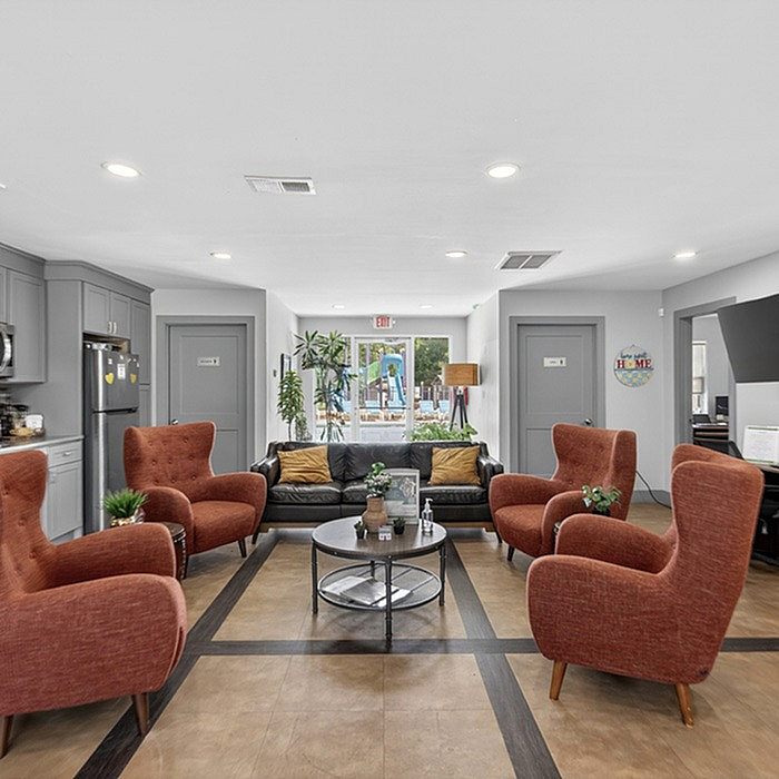 Inviting common area with stylish orange armchairs, sleek grey cabinets, and a view of the lush outdoor patio.