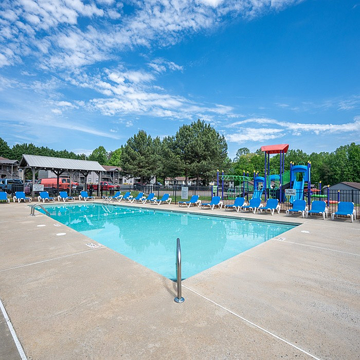 Inviting outdoor pool area with vibrant blue loungers and a charming playground, perfect for relaxation and family fun.