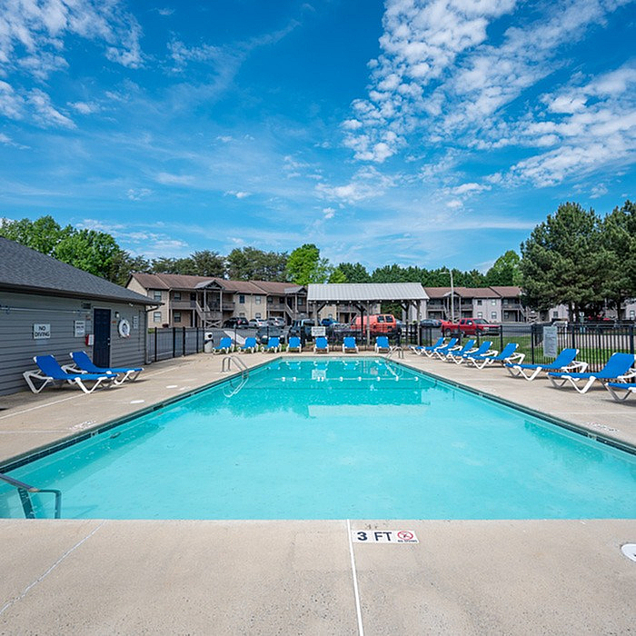 Inviting outdoor swimming pool with comfortable lounge chairs, surrounded by modern apartment buildings and lush greenery.
