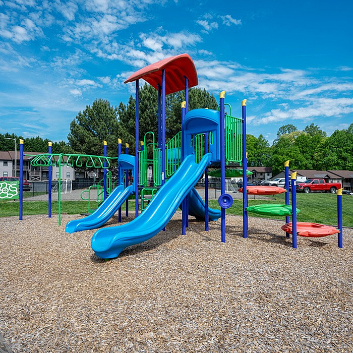 Bright and colorful playground with blue slides and climbing structures, set in a lush green community park.
