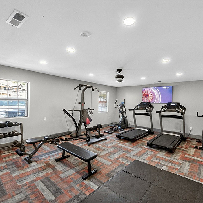 Bright and modern fitness room featuring state-of-the-art treadmills, weight benches, and a flat-screen TV for an energizing workout experience.