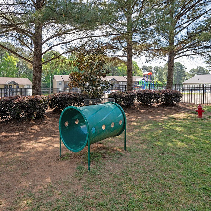 Scenic outdoor area with lush greenery, modern dog agility tunnel, and nearby community playground, perfect for pet-friendly living.