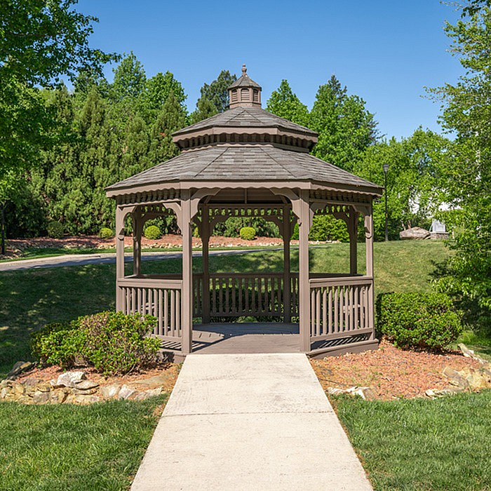 Charming wooden gazebo nestled in lush green garden setting beneath a clear blue sky, perfect for relaxation and outdoor gatherings.