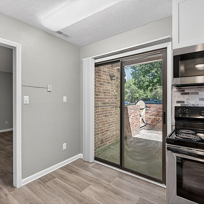 Bright and modern kitchen with sleek appliances, wood-style flooring, and a sliding glass door opening to a charming brick patio.