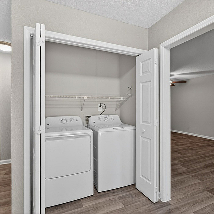 Charming in-unit laundry space with modern washer and dryer, adjacent to spacious room with sleek flooring.