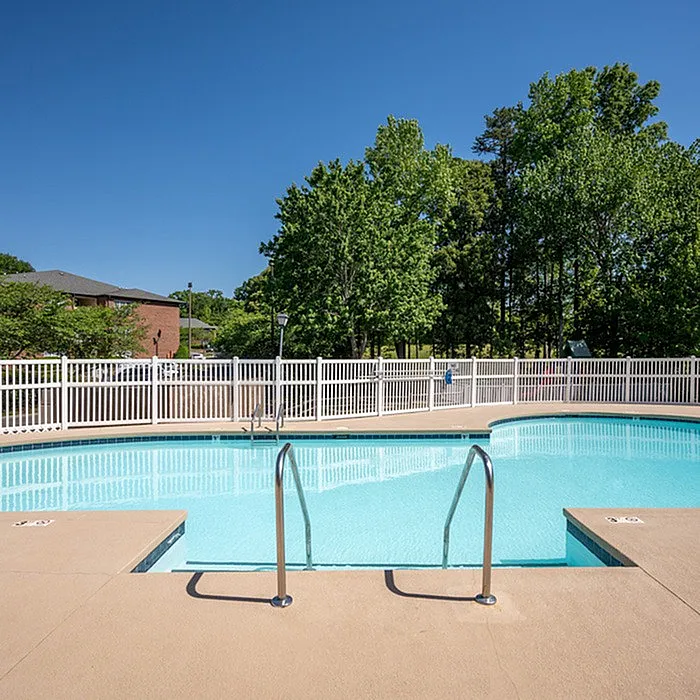 Inviting outdoor swimming pool with crystal-clear water, surrounded by lush greenery and a secure white fence, perfect for relaxation.