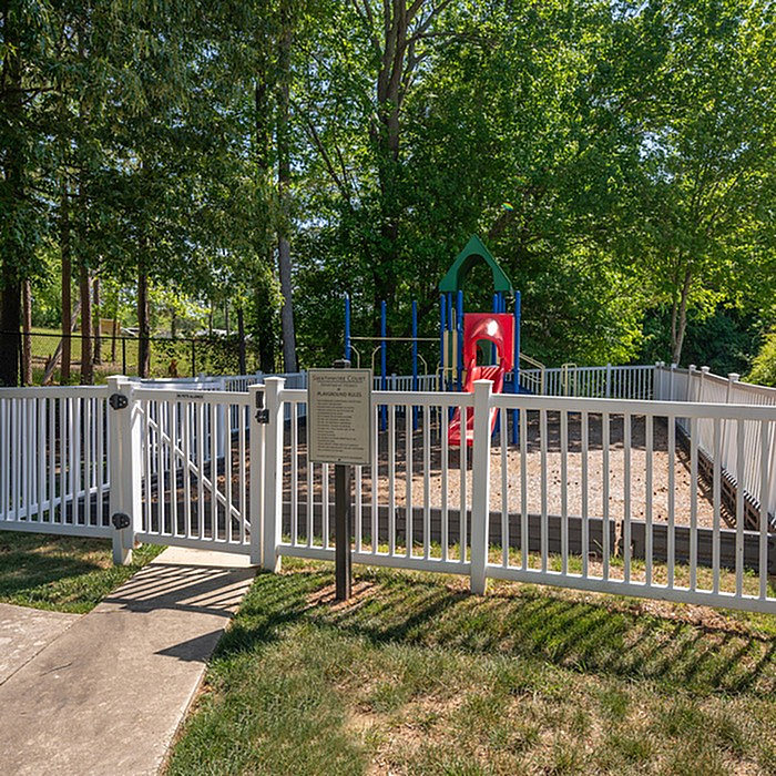 Charming fenced playground surrounded by lush greenery, featuring a vibrant slide and activity structure for kids.