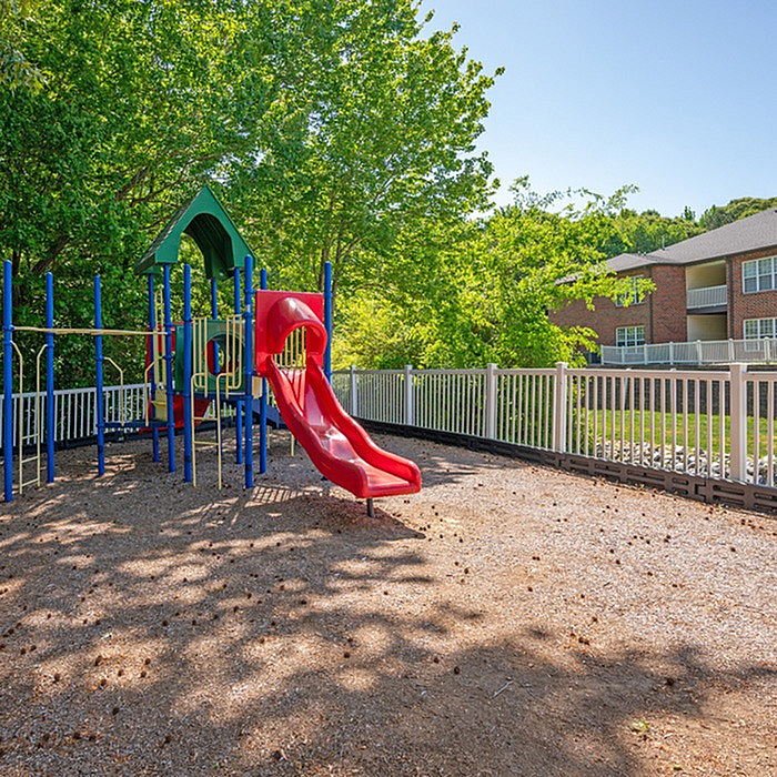 Inviting playground area with vibrant red slide and climbing structures, surrounded by lush greenery, perfect for family fun and relaxation.