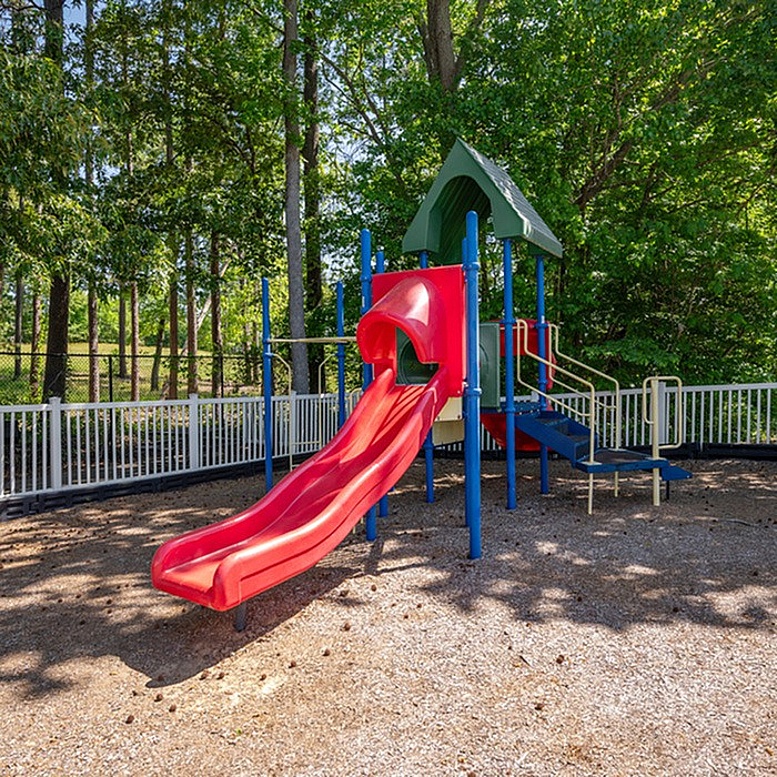 Charming playground with a vibrant red slide set amidst lush greenery, perfect for family-friendly outdoor fun.