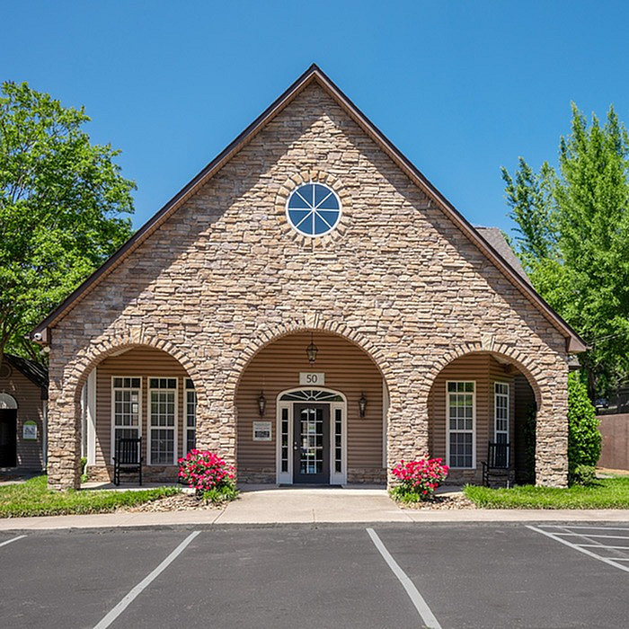 Charming apartment building with rustic stonework facade, arched entryway, and lush landscaping.