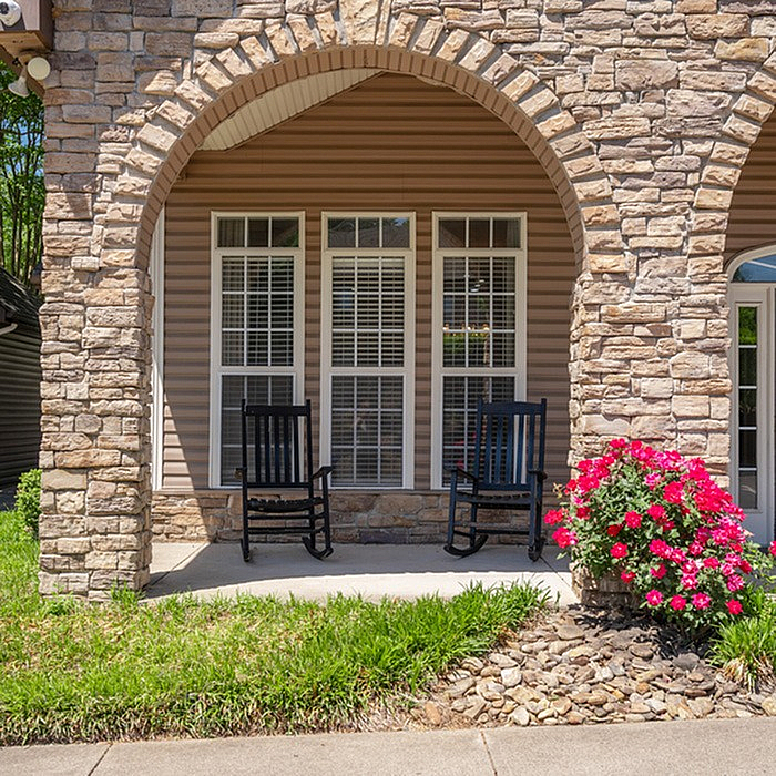Charming stone facade with elegant arches, rocking chairs, and vibrant flowers offering a welcoming front porch ambiance.