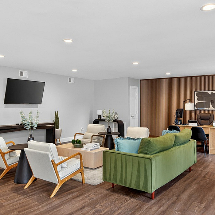 Modern living room with elegant decor, featuring a plush green sofa, stylish armchairs, sleek wooden flooring, and a contemporary wall design.