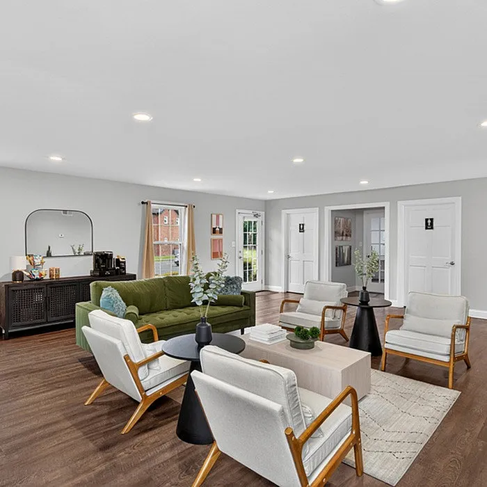 Bright and spacious living room with modern decor, featuring a green sofa, elegant armchairs, and a chic wooden floor, ideal for stylish living.