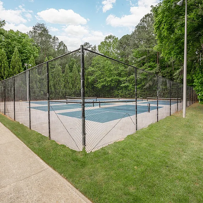 Inviting outdoor tennis court surrounded by lush green trees and clear blue skies, perfect for recreational activities.