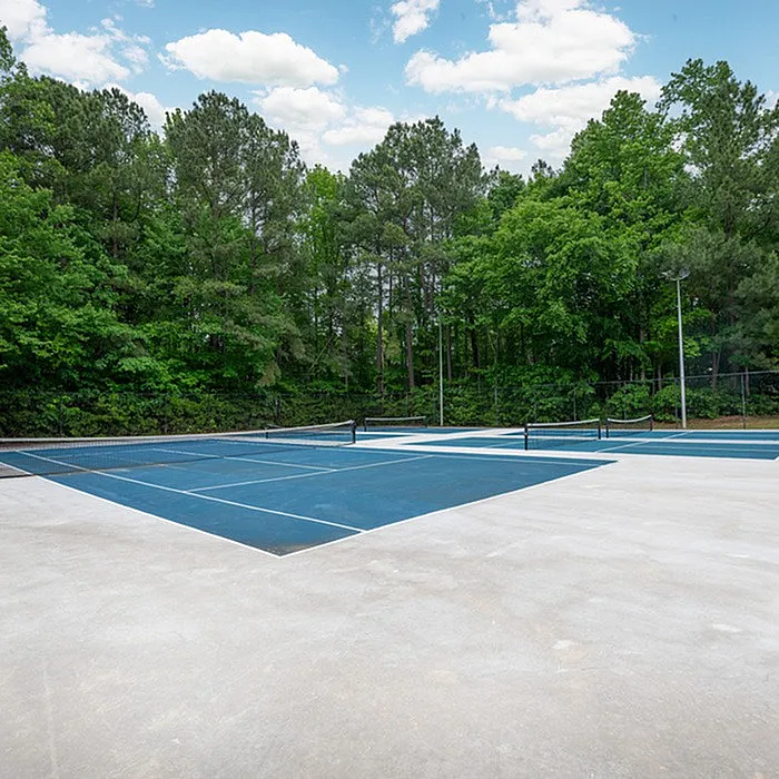 Inviting outdoor tennis court surrounded by lush greenery and serene trees, offering a perfect retreat for sports enthusiasts.