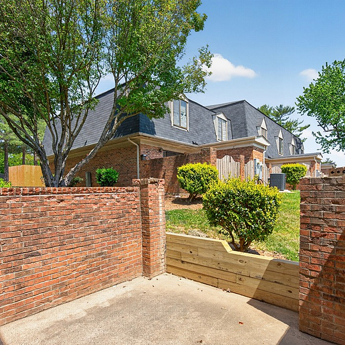 Charming townhouse exterior featuring classic brickwork, lush greenery, and a private fenced patio space.