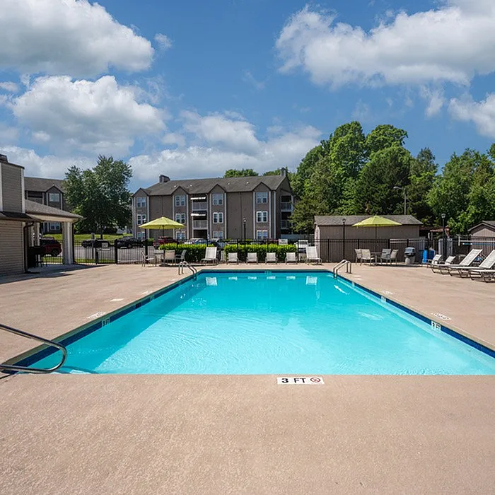 Inviting apartment complex with a sparkling pool, surrounded by lush greenery and comfortable lounging chairs.