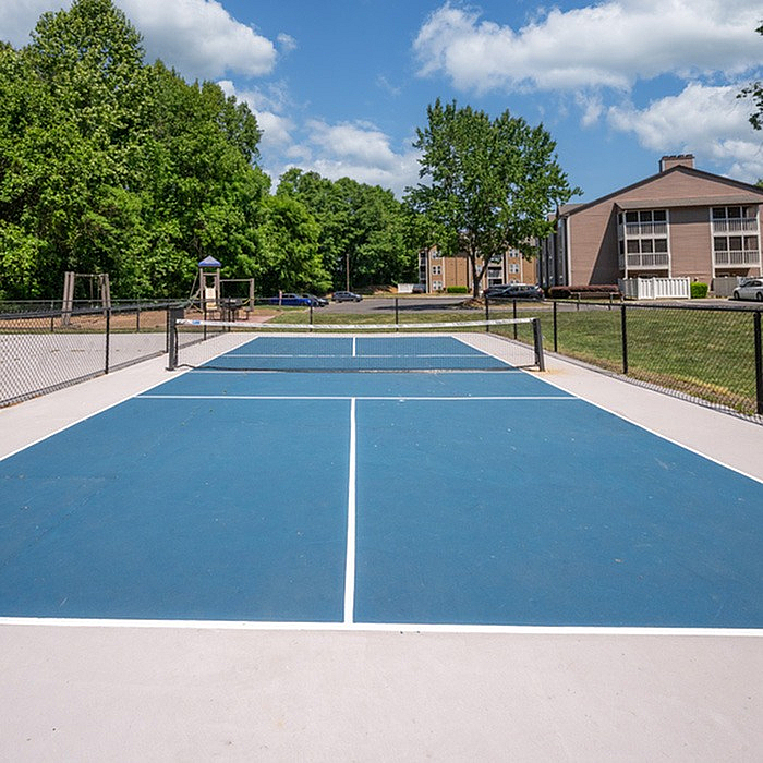 Vibrant apartment community features a pristine tennis court surrounded by lush greenery and modern buildings, perfect for sports enthusiasts.