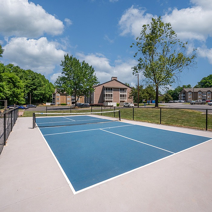 Vibrant outdoor tennis court in a serene residential setting, surrounded by lush greenery and modern apartments, perfect for active living.