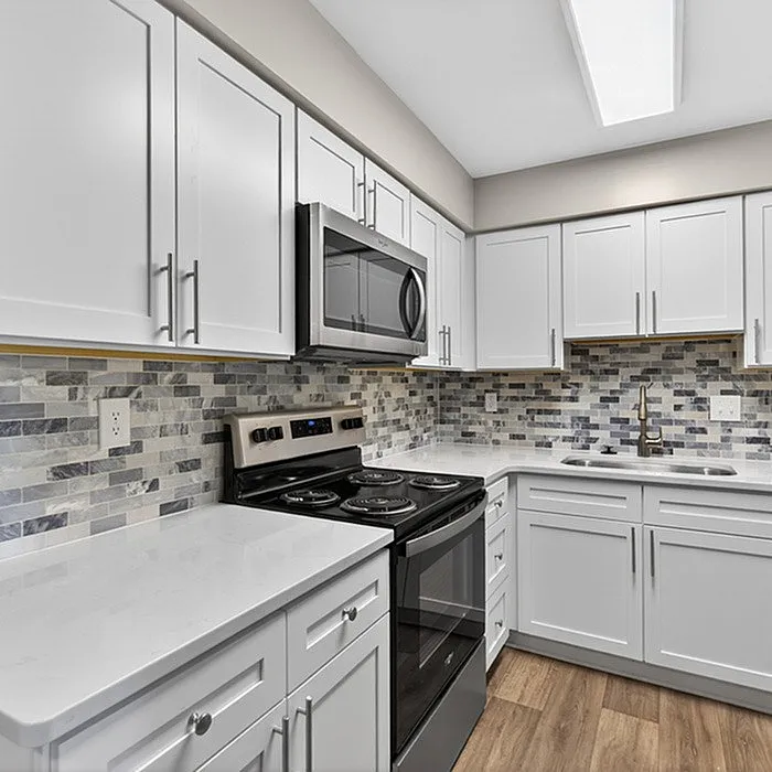 Elegant modern kitchen with sleek white cabinetry, stainless steel appliances, and a stylish tiled backsplash, perfect for culinary exploration.