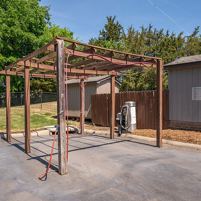 Charming outdoor car wash area with wooden canopy, surrounded by lush greenery, perfect for convenient vehicle maintenance.