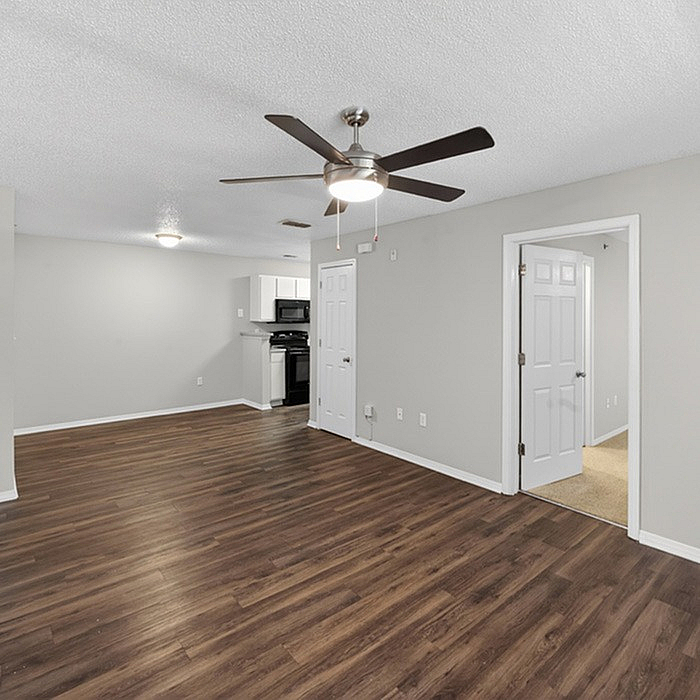 Modern apartment interior showcasing sleek wood flooring, a spacious open living area, and a contemporary kitchen with elegant ceiling fan lighting.