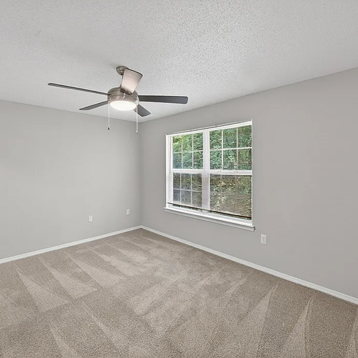 Bright bedroom with soft carpet, modern ceiling fan, and large window offering lush green views.