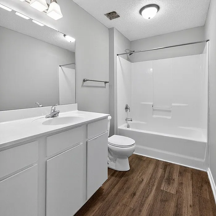 Bright modern bathroom with sleek white fixtures, elegant tub, and chic wood-style flooring.