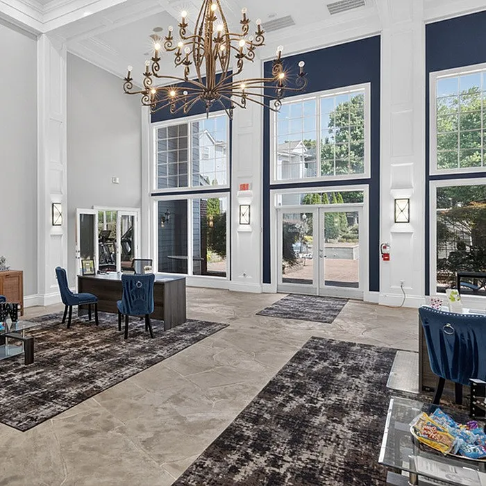 Elegant apartment lobby with grand chandelier, high ceilings, and large windows providing abundant natural light.