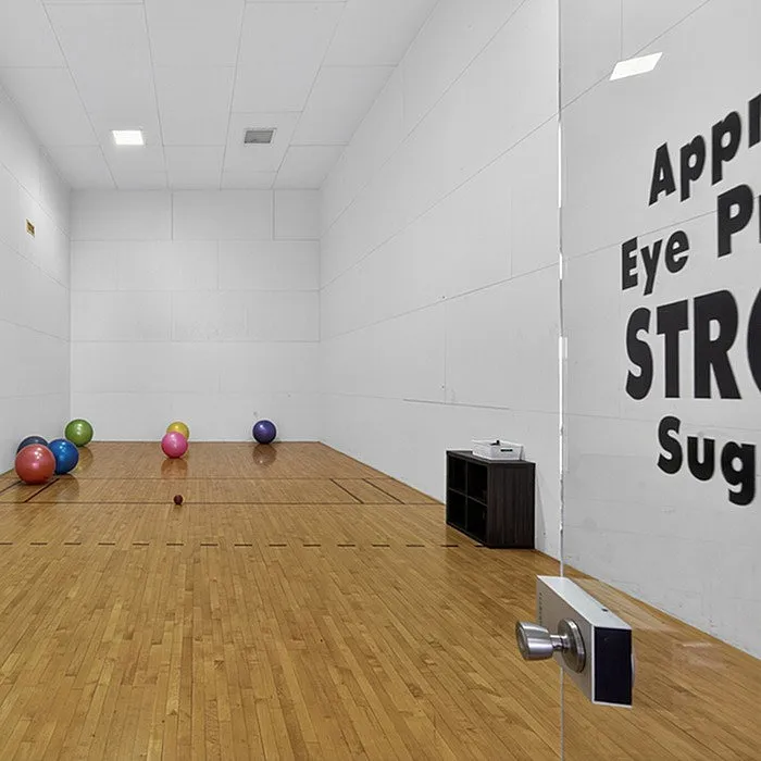 Bright and inviting indoor racquetball court with polished wooden floors and colorful exercise balls, perfect for an energetic workout or leisure play.