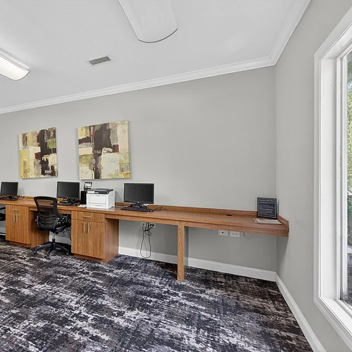 Modern workspace with sleek wooden desks, contemporary chairs, and dual computer setups, enhanced by abstract wall art and ample natural light.