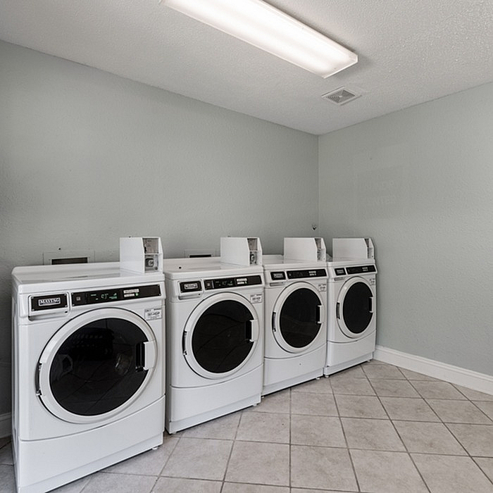 Modern laundry room with four sleek white washing machines set against a calming light grey wall, perfect for convenient living.