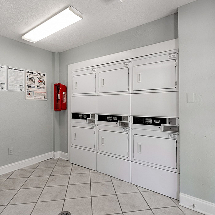 Bright and efficient laundry room with modern, stacked washers and dryers, tiled flooring, and clear usage instructions for convenience.