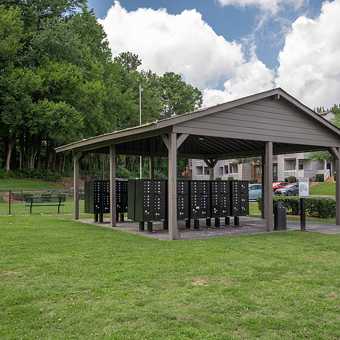 Charming outdoor pavilion with secure mailboxes, nestled in a lush green landscape, perfect for a serene apartment community setting.