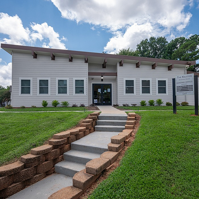 Inviting leasing office exterior with modern design, surrounded by lush greenery and clear skies.