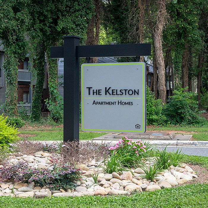 Inviting entrance sign of The Kelston Apartment Homes, surrounded by lush greenery and a serene landscape.