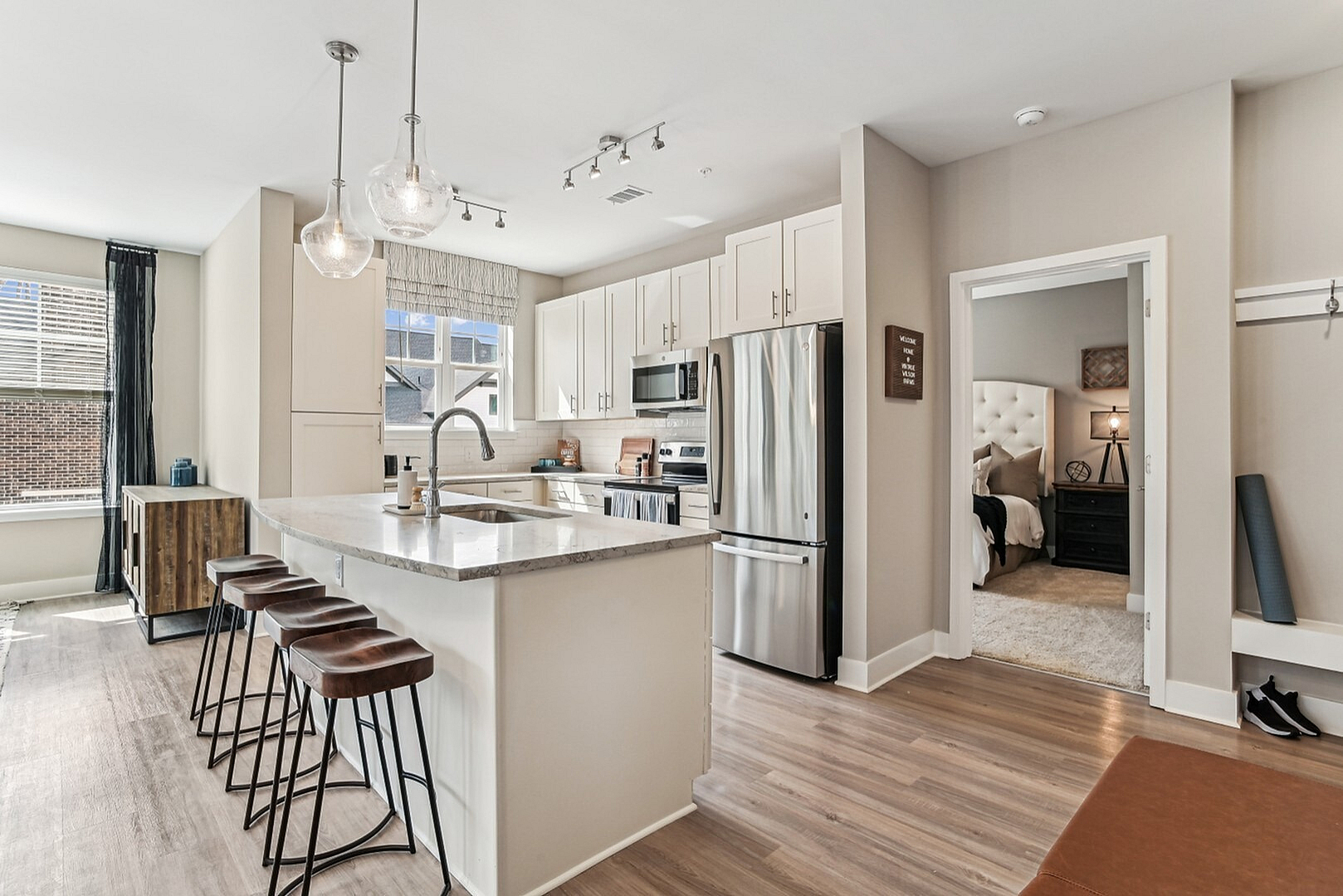 Contemporary open kitchen with elegant island, chic pendant lighting, stainless steel appliances, and inviting bar seating leading to a cozy bedroom.