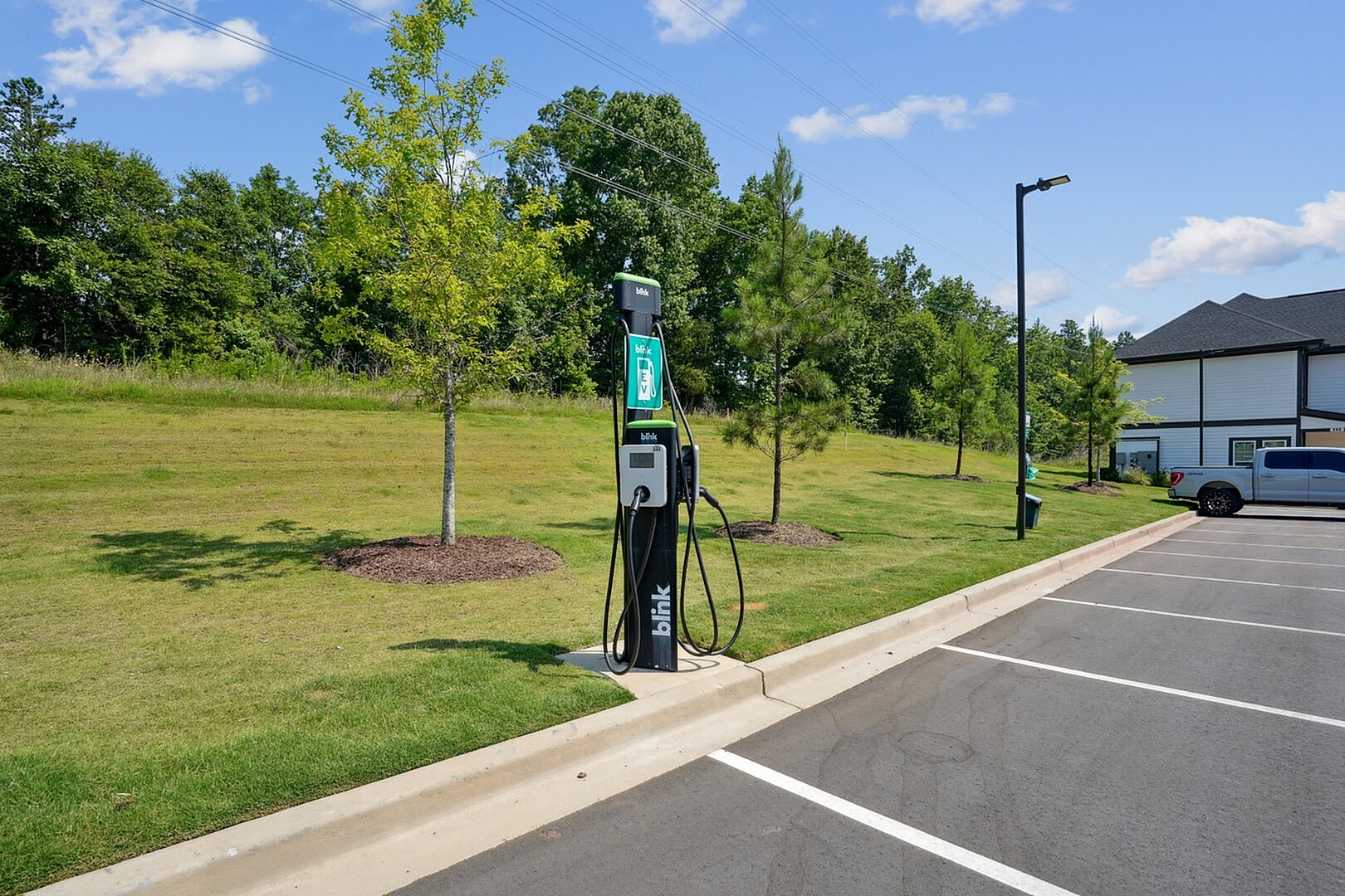 Eco-friendly apartment complex parking lot featuring a Blink electric vehicle charging station and lush green landscaping.
