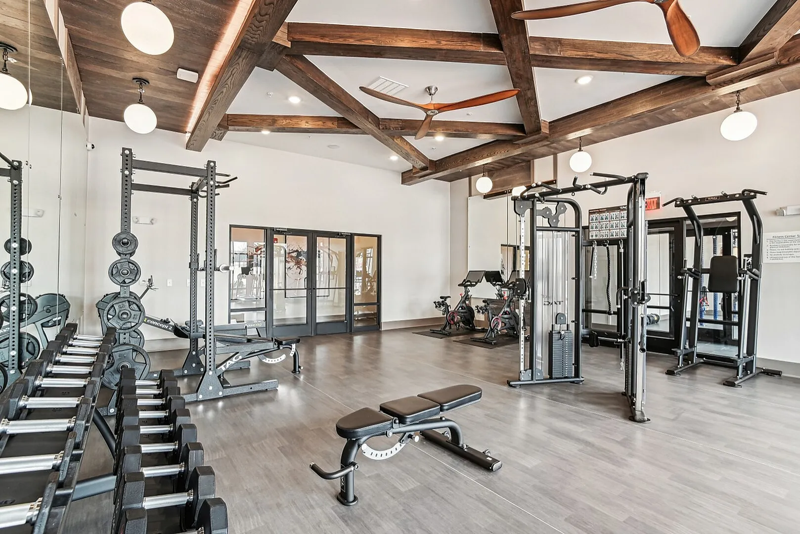 Modern fitness center with state-of-the-art equipment, including free weights, strength machines, and spin bikes, under elegant wood ceiling beams.