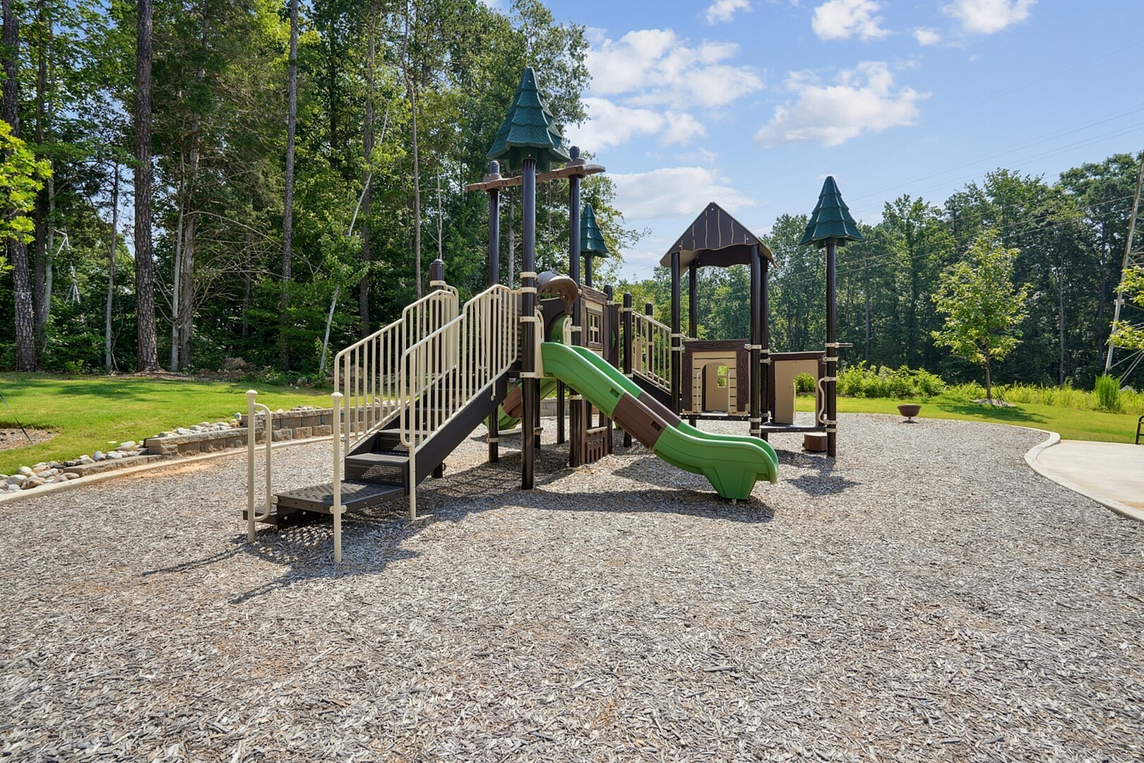 Charming play area with modern playground equipment nestled in a serene, wooded setting, perfect for family fun.