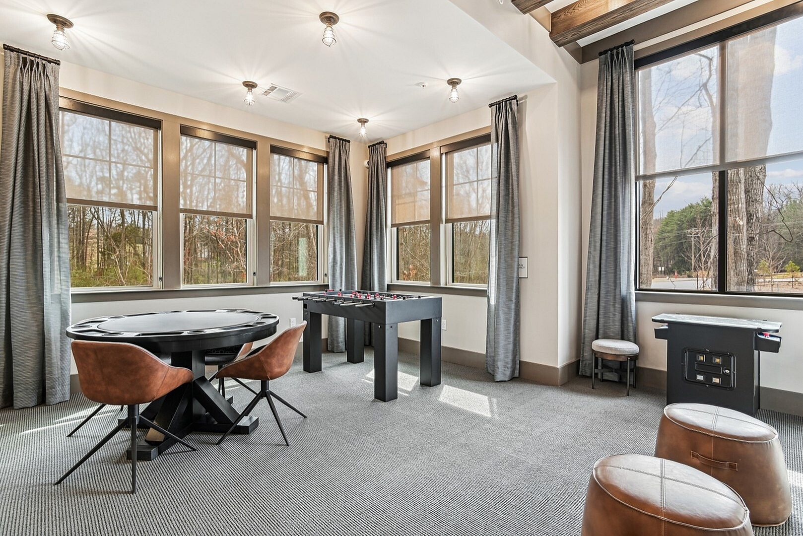 Inviting recreation room with large windows, modern foosball table, stylish poker table, and cozy seating, perfect for entertainment and relaxation.