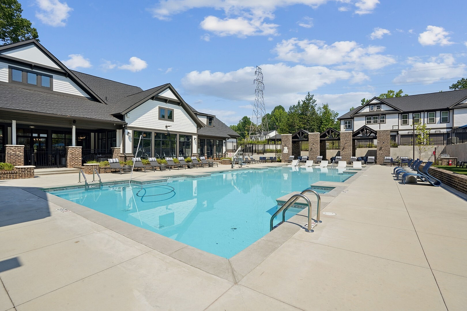 Luxurious apartment complex showcasing a sparkling pool with lounge chairs, modern clubhouse, and lush surroundings, offering a perfect blend of relaxation and style.