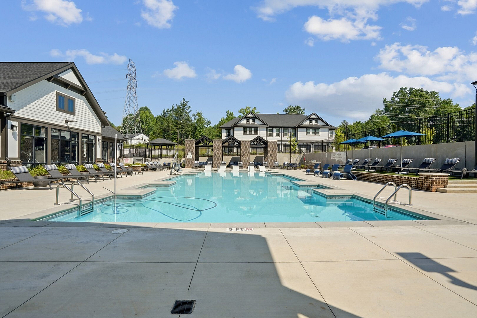 Luxurious apartment complex featuring a sparkling swimming pool surrounded by elegant lounge chairs and vibrant greenery.