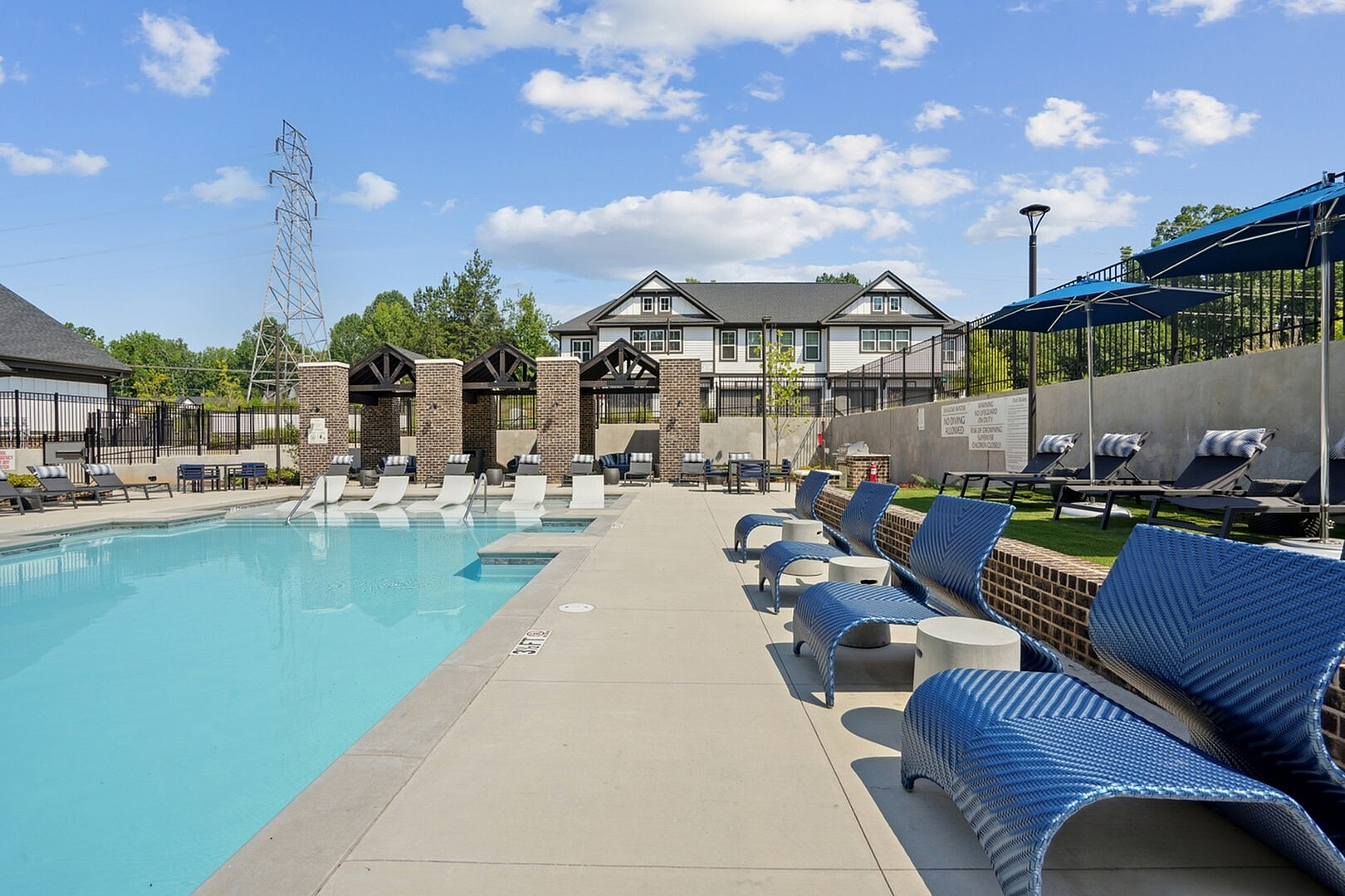 Luxurious apartment complex with a refreshing outdoor pool, stylish lounge chairs, and elegant brick architecture under a bright blue sky.