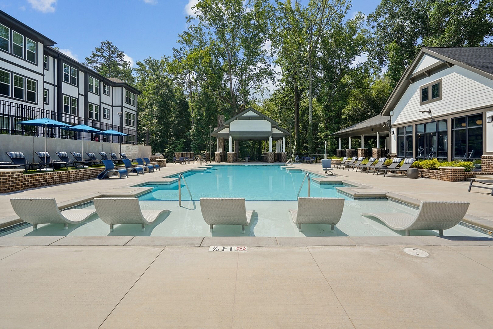 Luxurious apartment complex featuring a serene outdoor pool area with stylish lounge chairs and a modern clubhouse under a clear blue sky.
