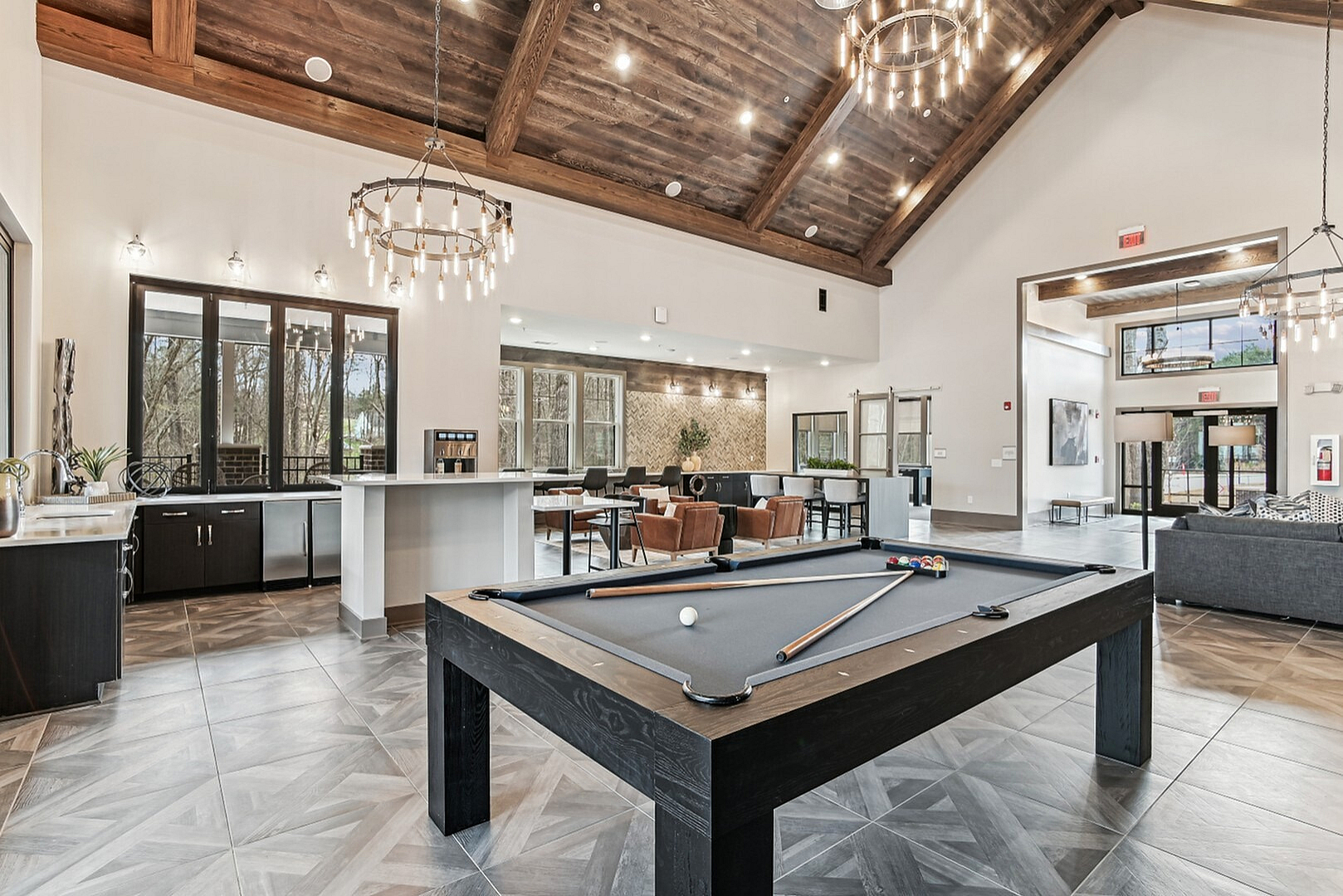 Elegant residential recreation space featuring a spacious lounge with a modern pool table, stylish chandeliers, ample natural light, and a cozy seating area.