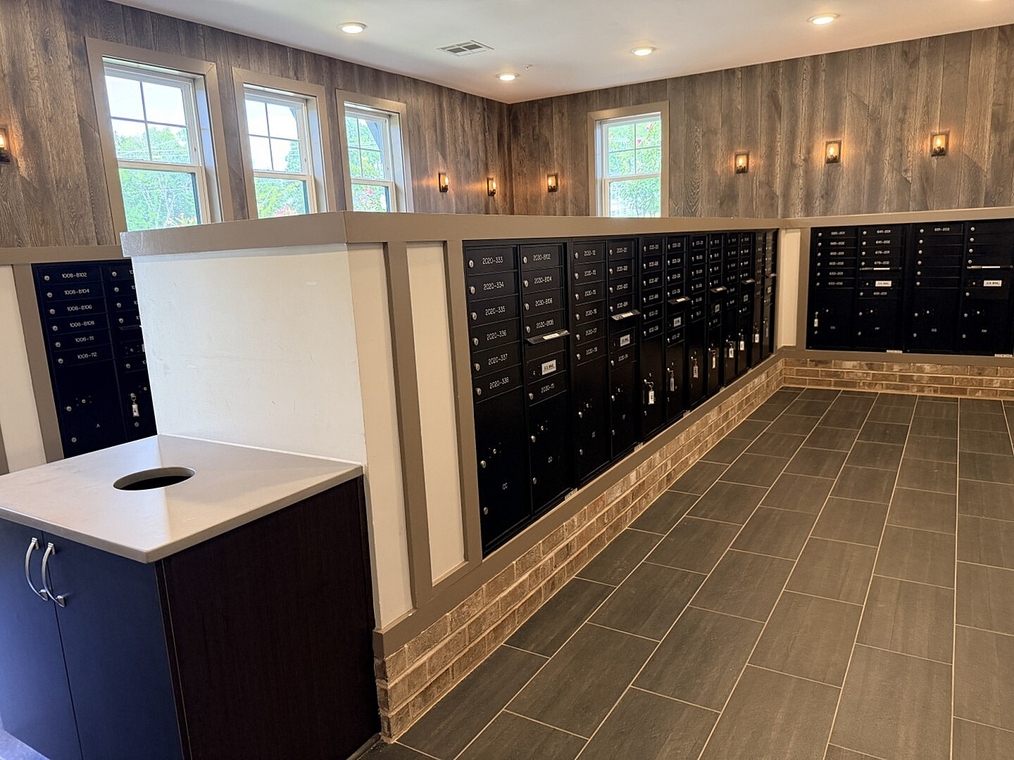 Elegant mailroom with stylish tile flooring, modern wall lights, and an array of secure black mailboxes, offering a blend of functionality and contemporary design.