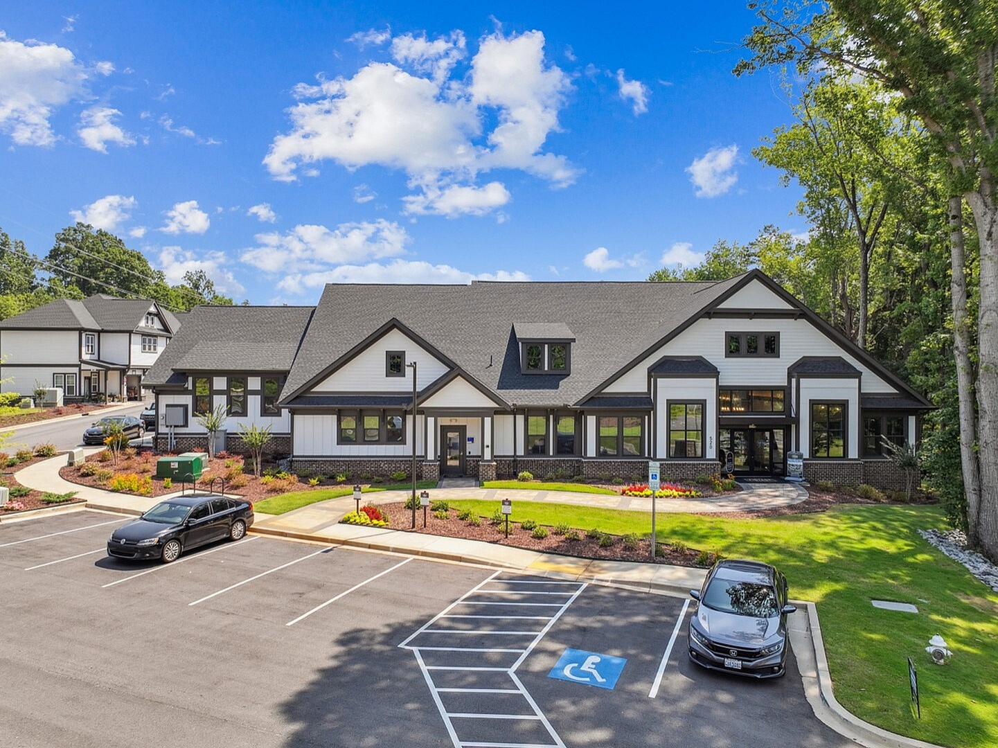 Charming two-story community building surrounded by lush greenery and well-maintained parking space under a bright blue sky.