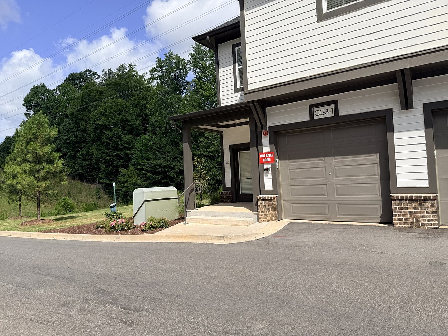 Inviting townhouse exterior with modern garage and charming landscaping, set against lush green surroundings.