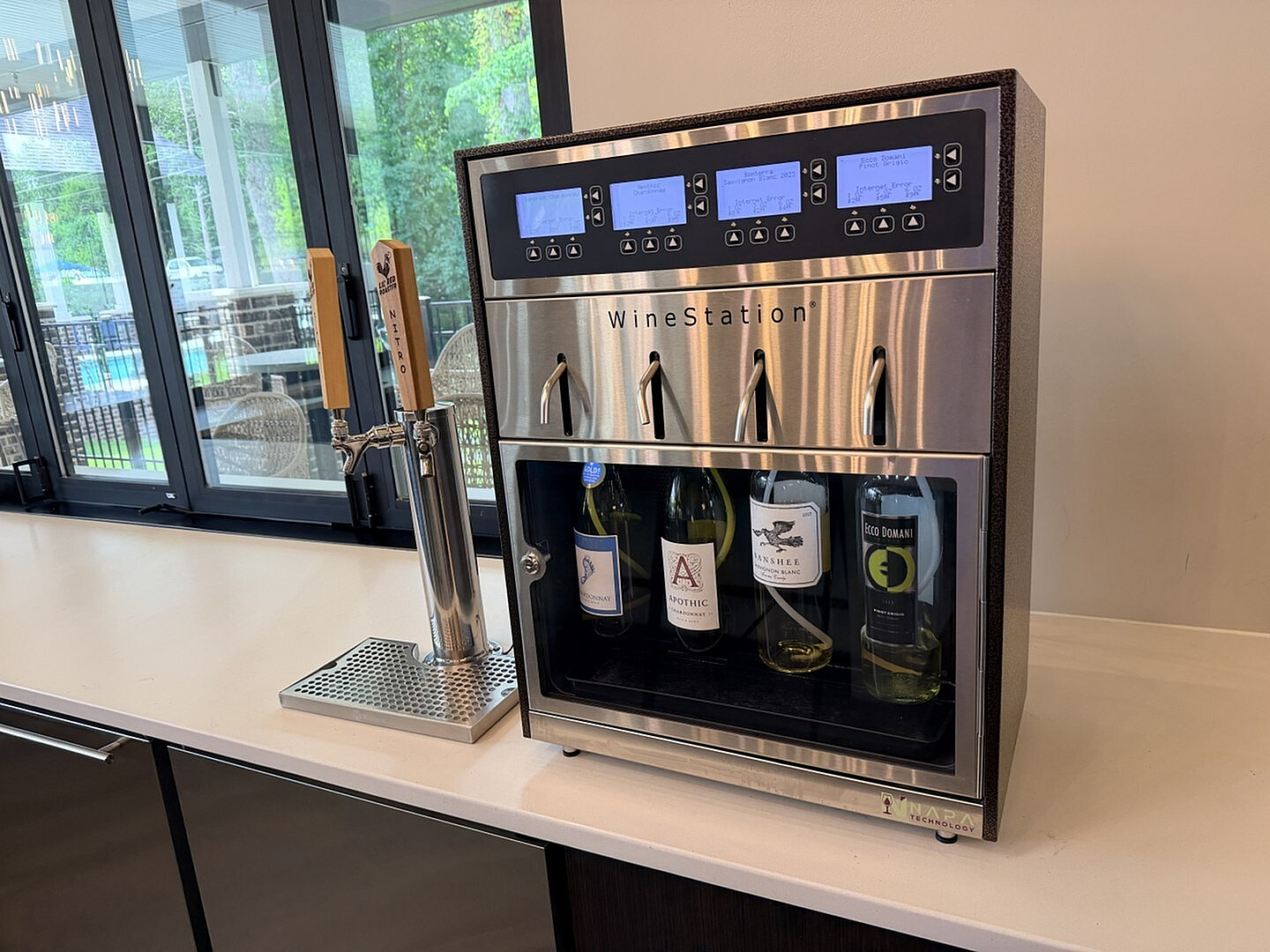 Modern kitchen with a sleek wine dispenser and lush green scenery visible through large windows, enhancing the space's luxury appeal.